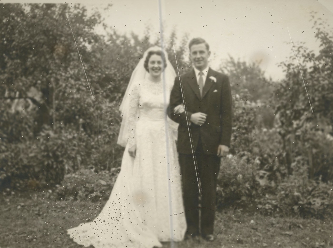 A photograph in the style of a 1955 wedding print, black and white and badly aged, with dust, brown spots, a crease and scratch lines across it.