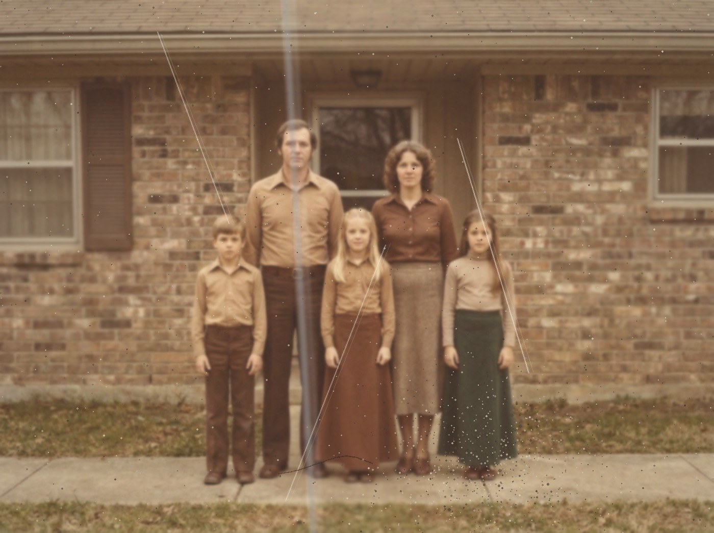A photograph in the style of a 1978 colour print: a family of five, faded, with dust, brown spots and scratch lines across it.