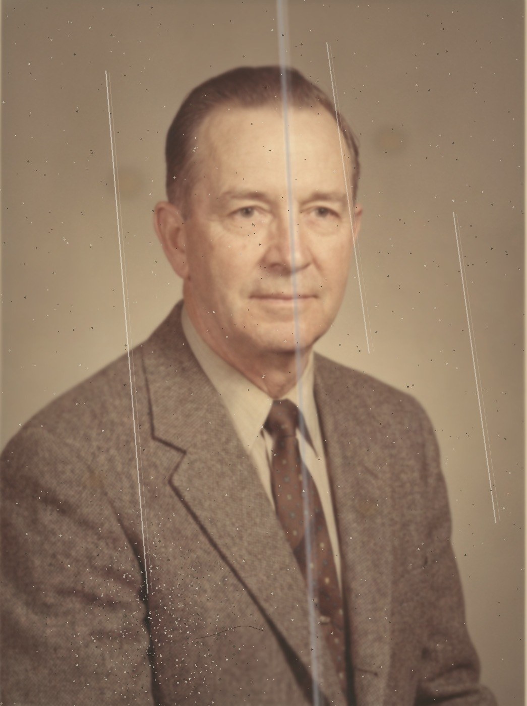 A photograph in the style of a 1958 studio portrait: a man in a jacket and tie, speckled, faded and marked by scratch lines.