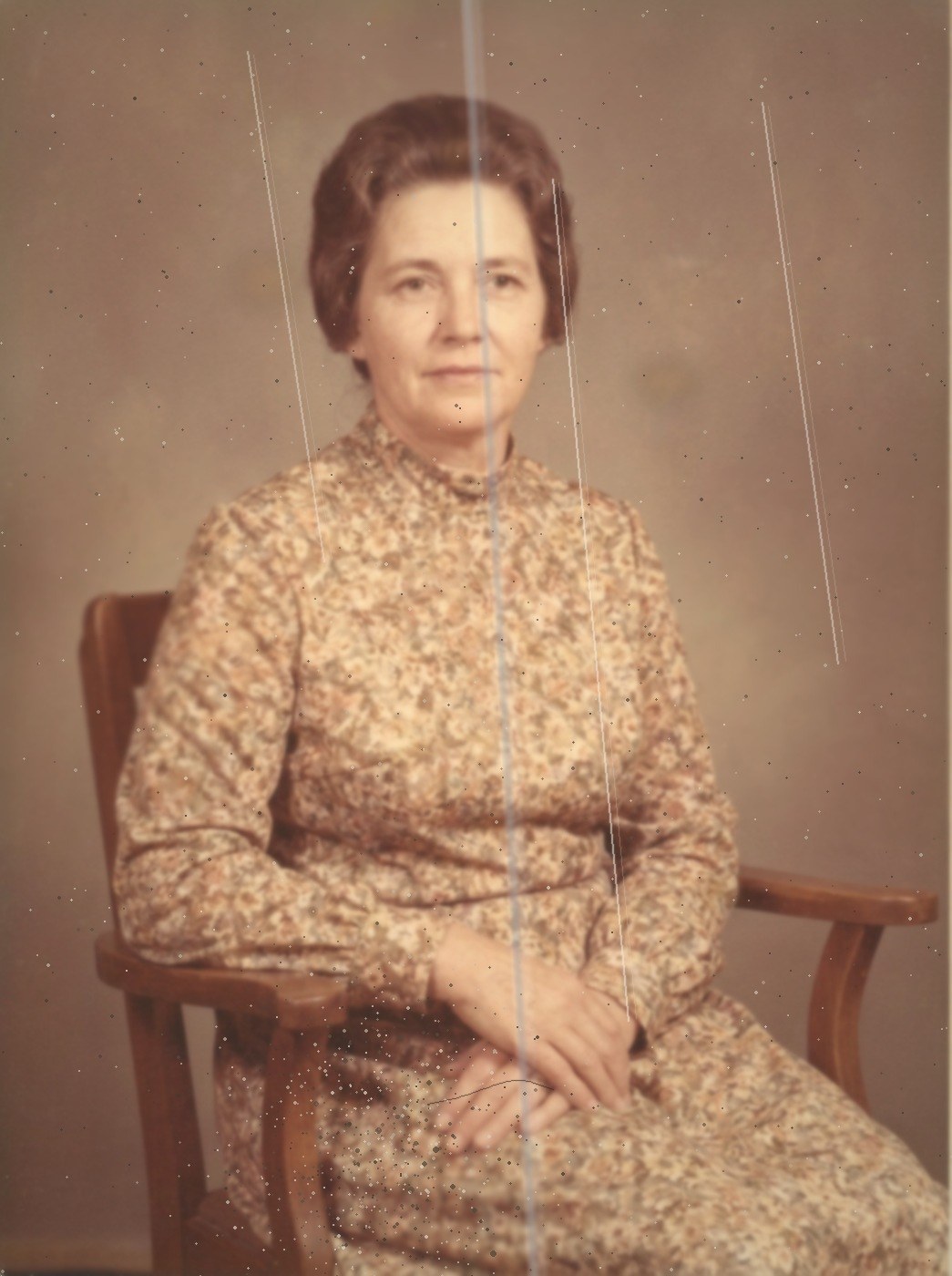 A photograph in the style of a 1968 studio portrait: a woman seated, faded and marked by dust, brown spots, a crease and scratch lines.